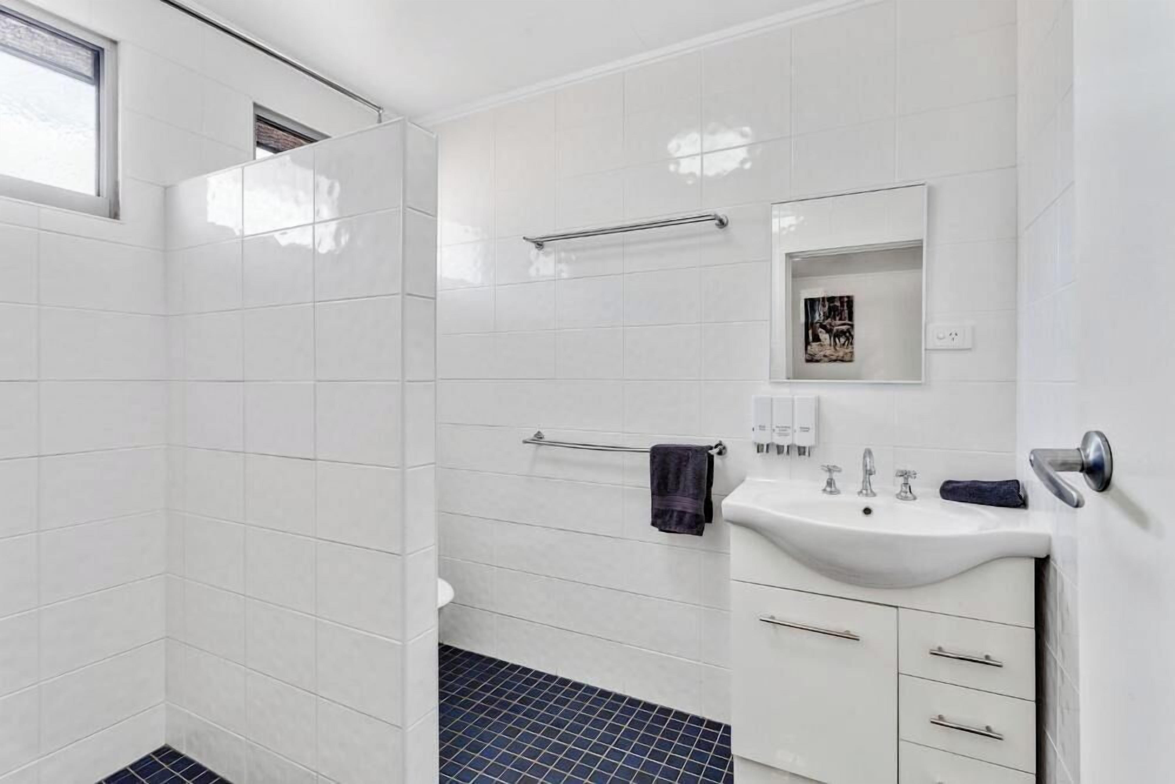 Un bagno moderno con piastrelle bianche, un lavandino, uno specchio e un porta asciugamani.