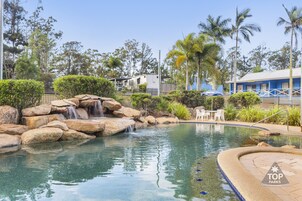 A pool area with a waterfall, surrounded by palm trees and a fence.