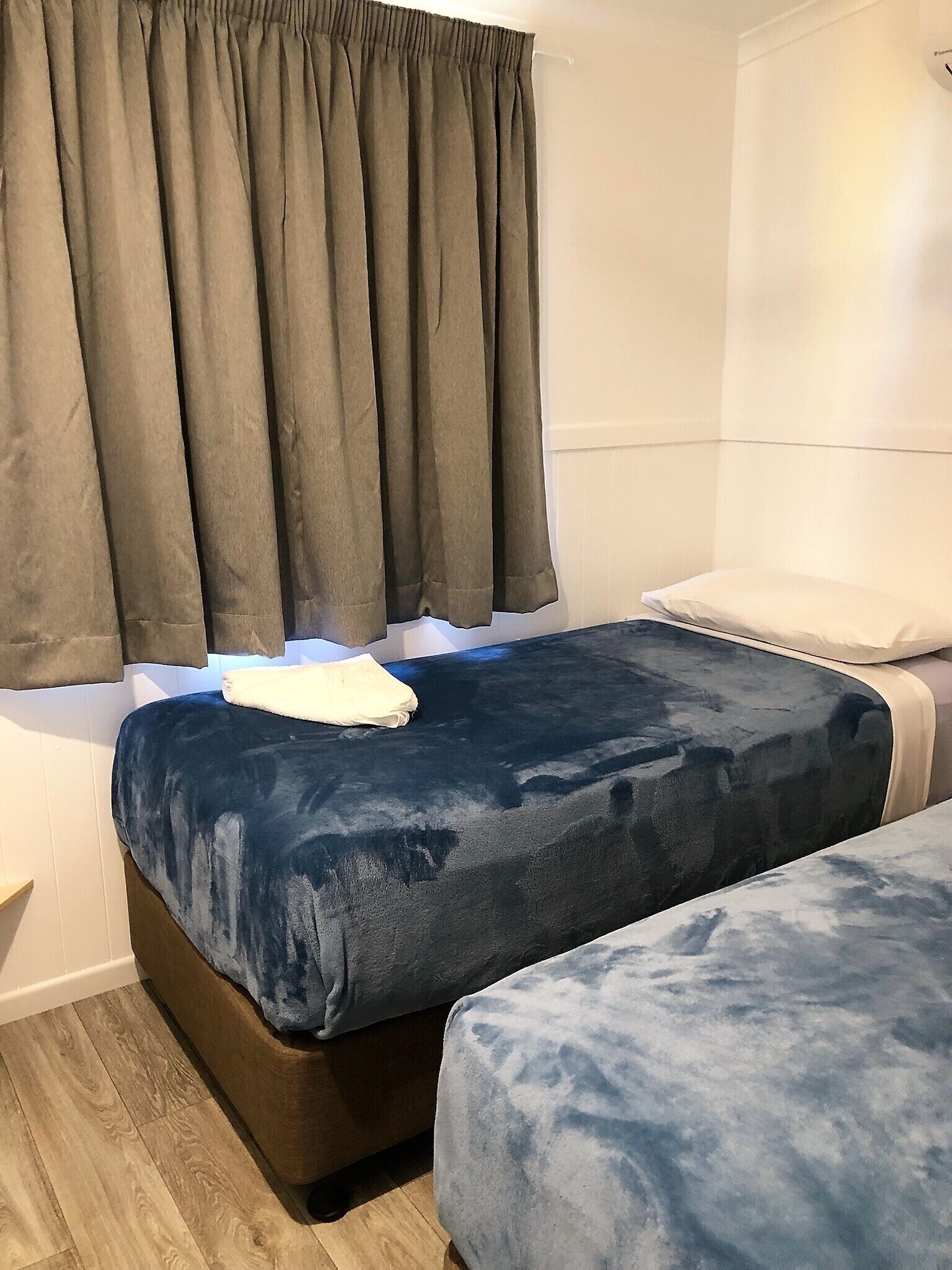 A room with two beds, a dark blue bedspread, a white pillow, and a brown headboard.