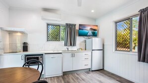 Une cuisine compacte avec des meubles blancs, un four à micro-ondes, un lave-vaisselle et un coin repas comprenant une table et des chaises en bois.