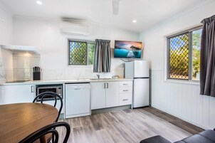 Una cocina funcional con armarios blancos, microondas, lavavajillas y comedor con mesa y sillas de madera.