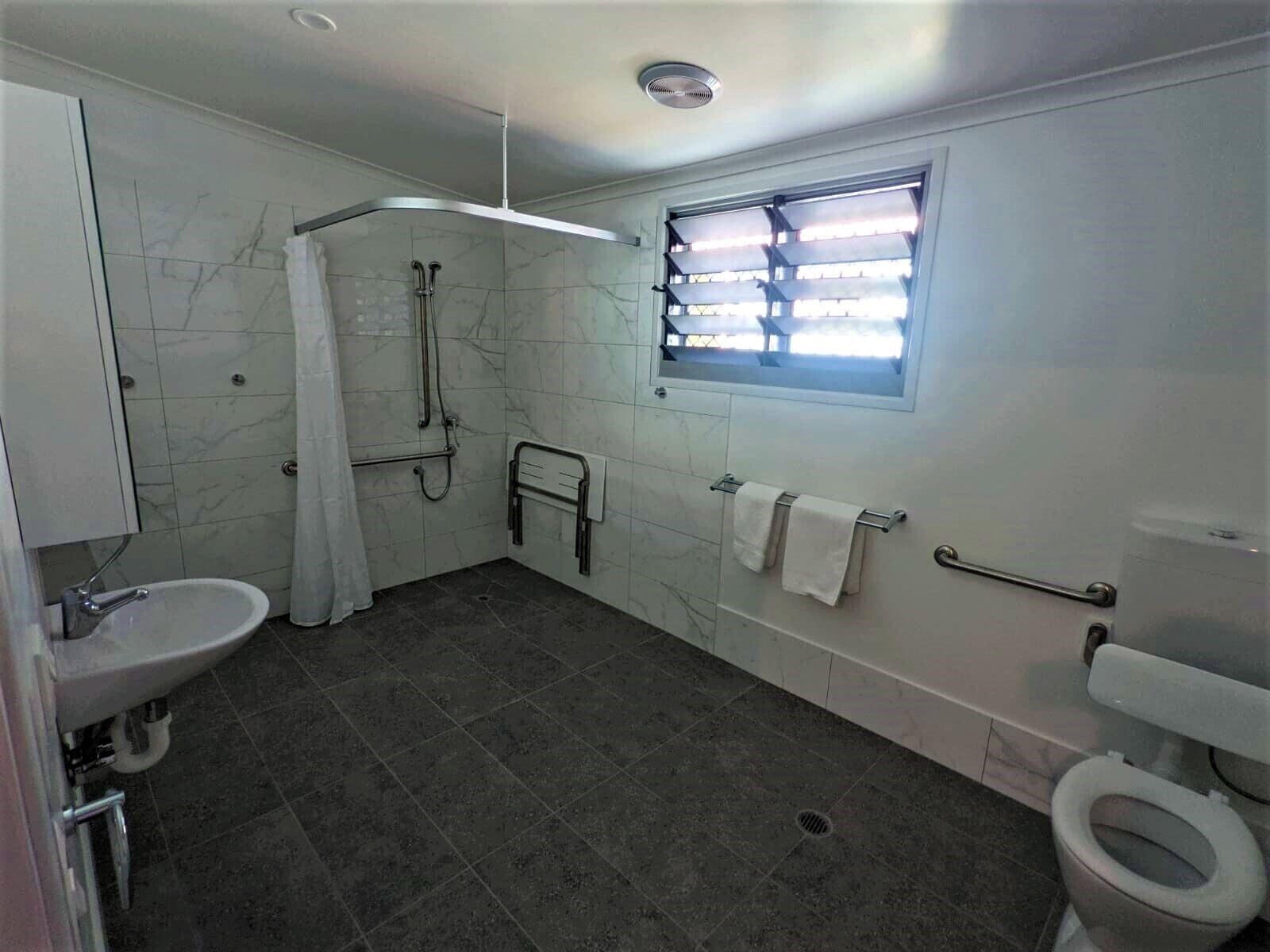 Baño con ducha, inodoro, lavabo y ventana con persianas.