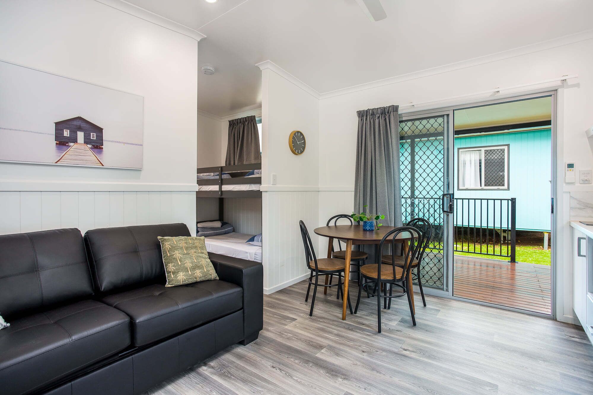 A compact living space with a black leather sofa, a dining table with chairs, and a small kitchen area.