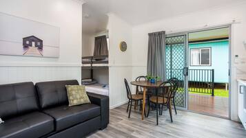 A compact living space with a black leather sofa, a dining table with chairs, and a small kitchen area.