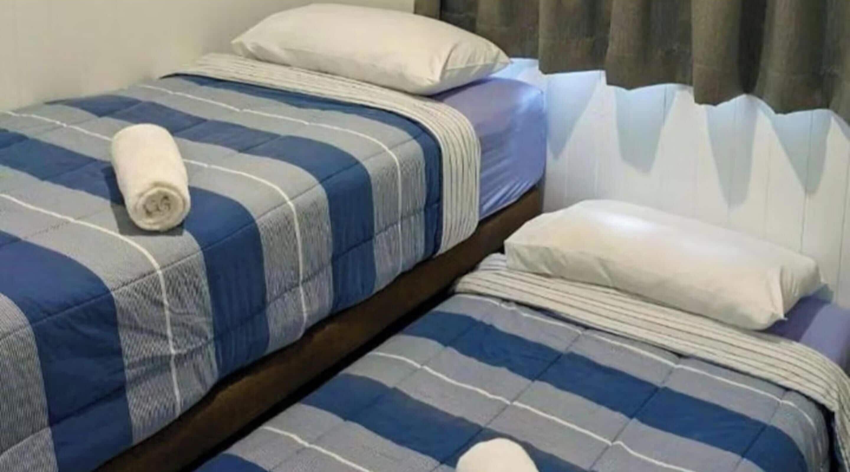 Two single beds with striped bedding, pillows, and a rolled-up towel.