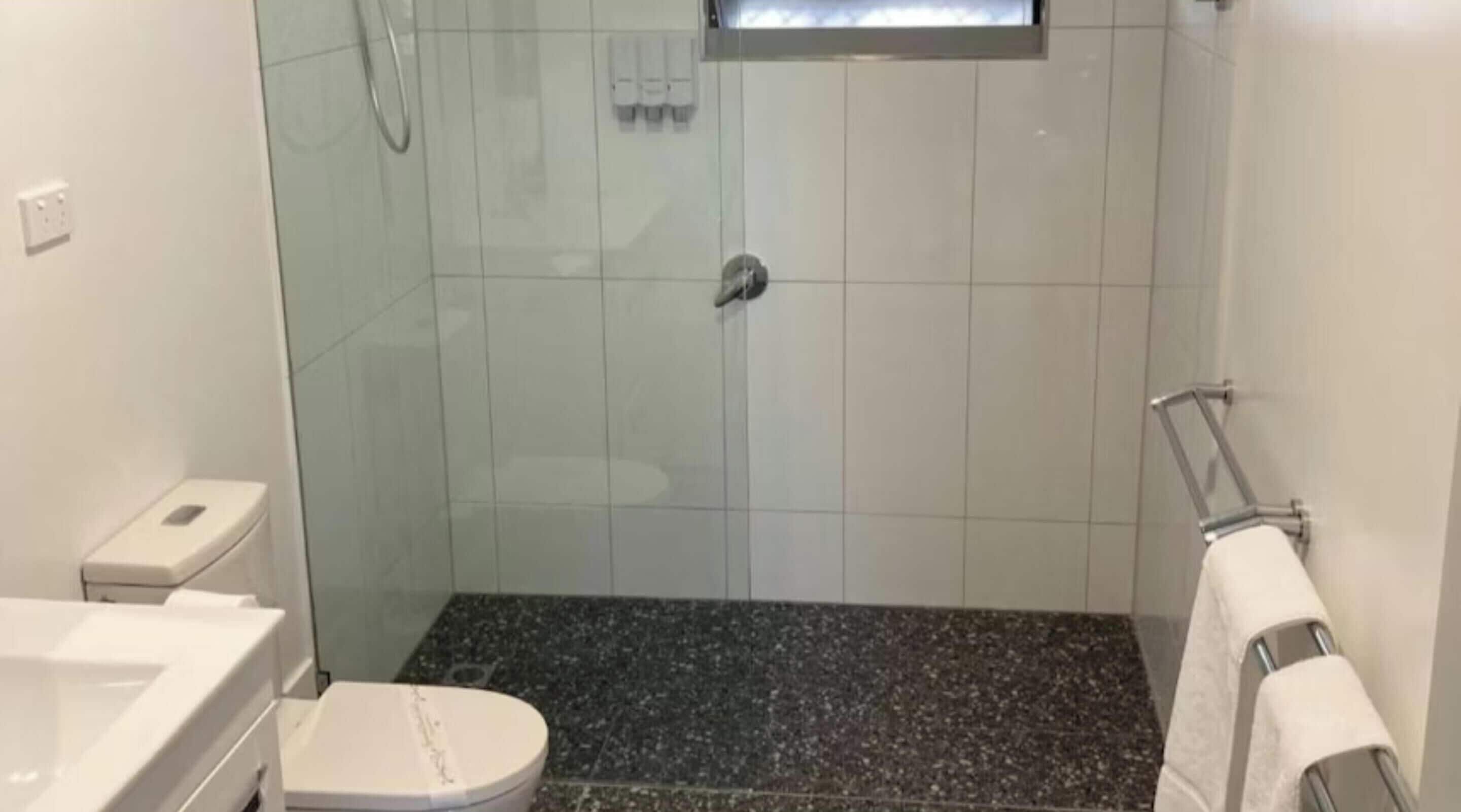 Ein Badezimmer mit weißer Toilette, einer Duschkabine mit Glastür und einem Granitboden.