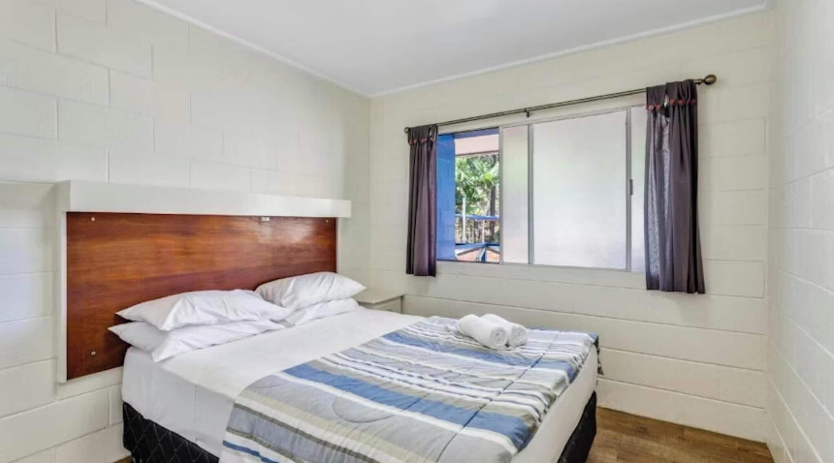 Una cama individual con cabecera de madera, ropa de cama blanca y una ventana con cortinas.