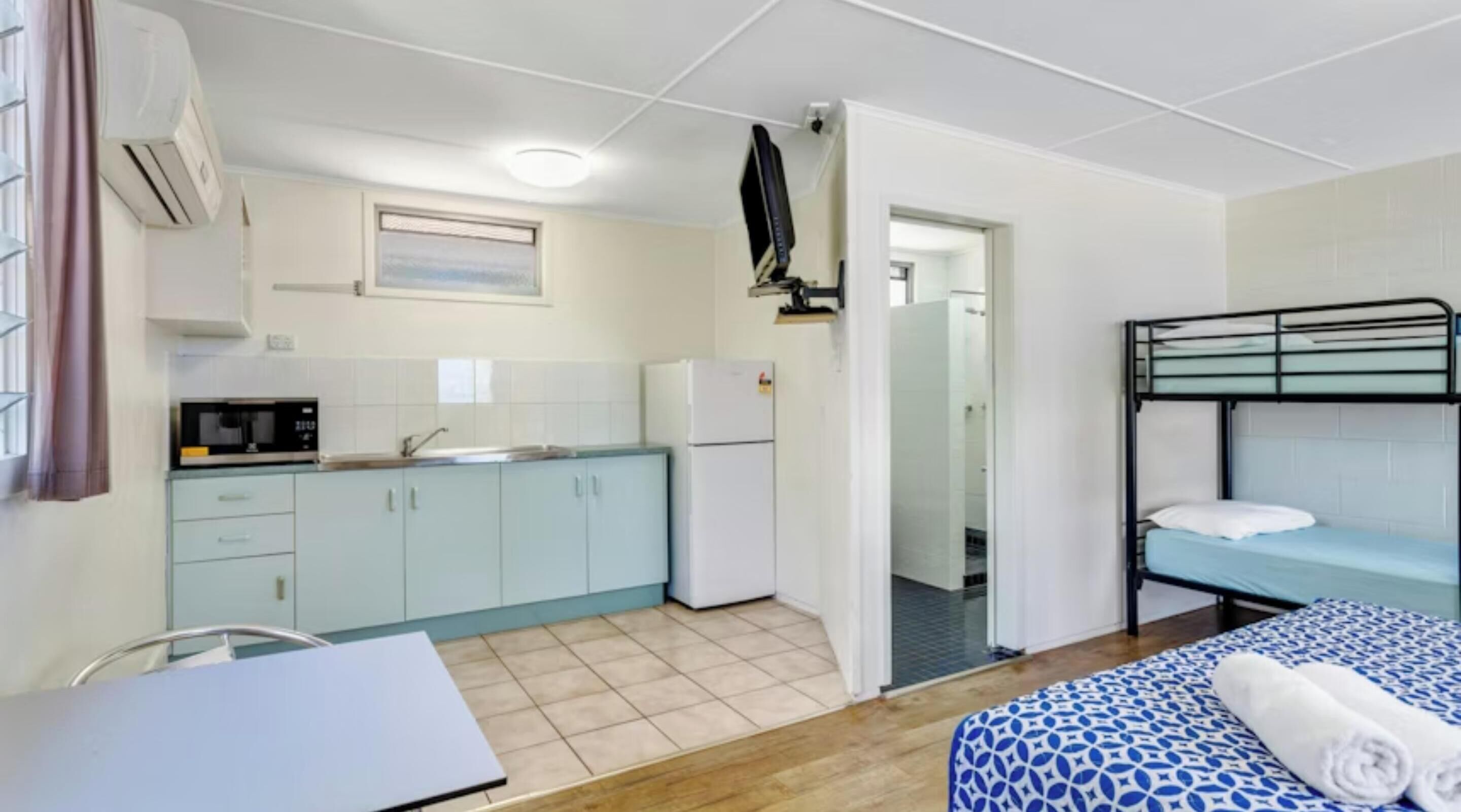 A compact room with a kitchenette, a bed with a patterned bedspread, and a desk with a laptop.