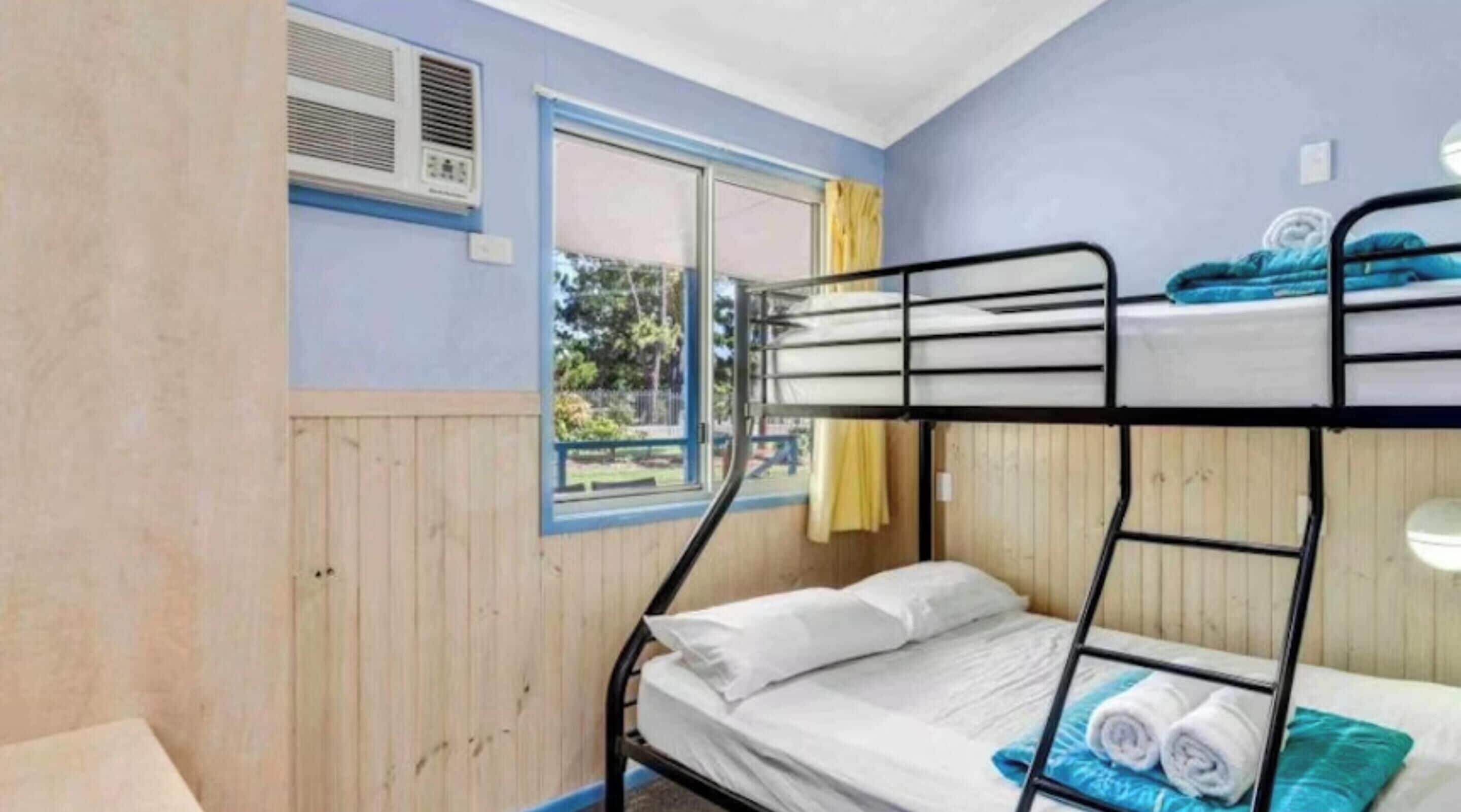 Quarto com beliche, ar condicionado na parede e vista para o exterior.