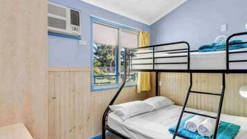 Quarto com beliche, ar condicionado na parede e vista para o exterior.
