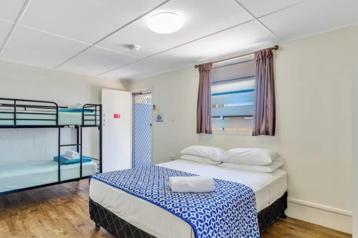 A room with bunk beds, a single bed, a window with curtains, and a door.