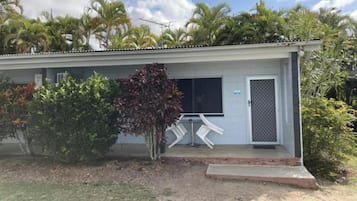 A single-story building with a flat roof, a door with a security screen, and a small porch area with two chairs.
