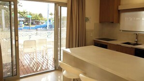 Une cuisine moderne dotée d’un grand îlot central, d’une porte-fenêtre coulissante donnant sur une terrasse extérieure et offrant une vue sur un parc aquatique.