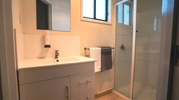 Un baño moderno con tocador blanco, cabina de ducha de vidrio y ventana que aporta luz natural.