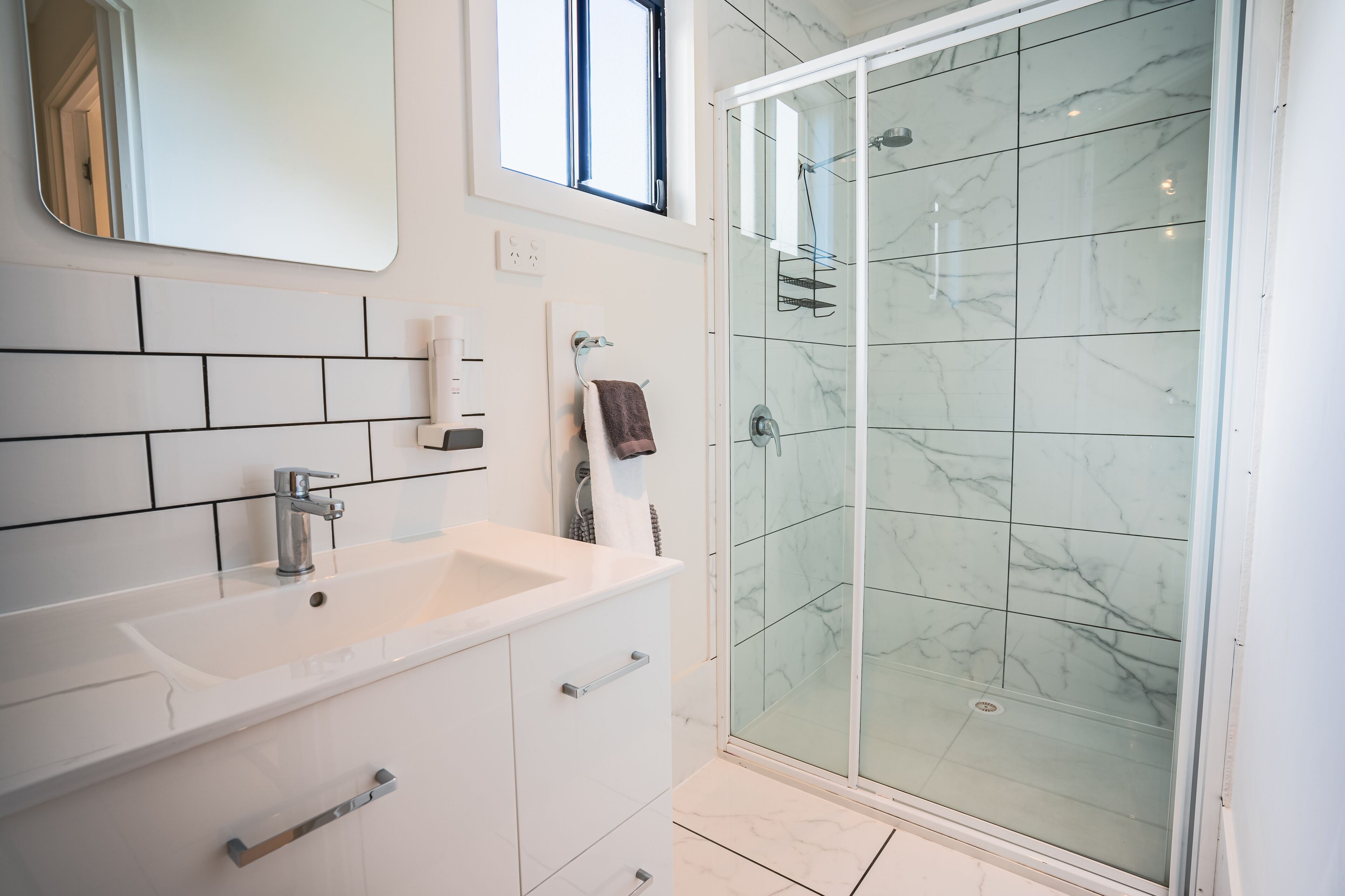 A modern bathroom with a white sink, mirror, and glass shower enclosure.