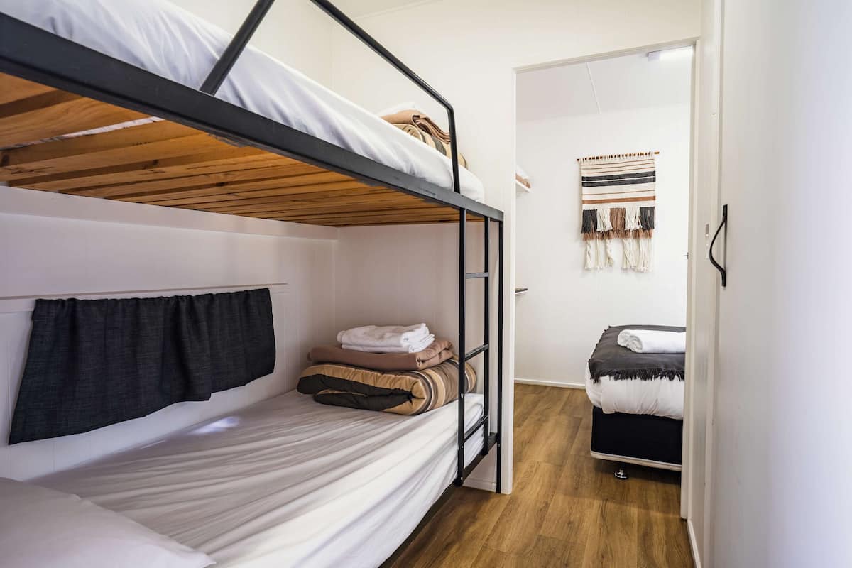 Quarto com beliche, teto de madeira, porta que dá para outro quarto e tapeçaria na parede.