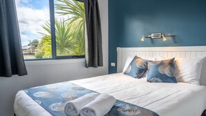 Una cama bien tendida con una colcha de diseño azul y blanco, dos almohadas y dos toallas enrolladas.