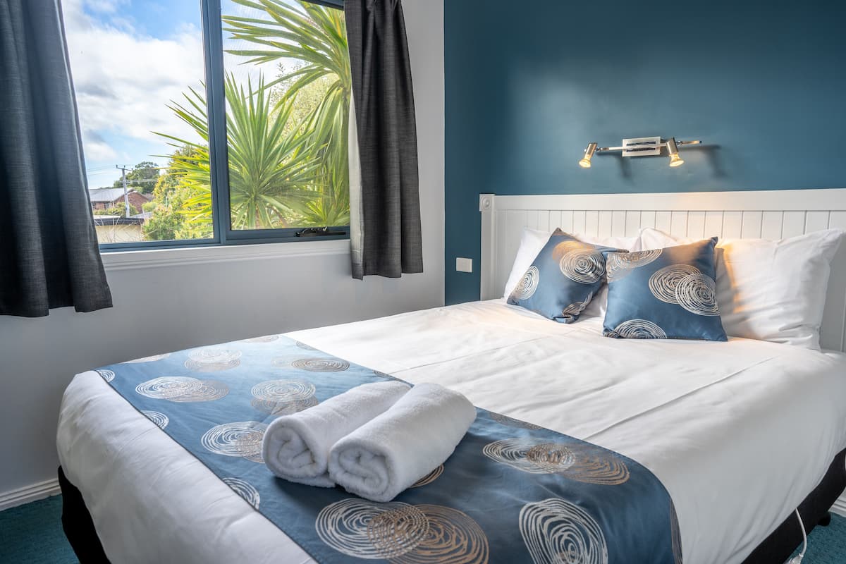 Cama bem arrumada com colcha azul e branca estampada, dois travesseiros e duas toalhas enroladas.
