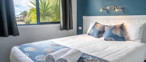 A neatly made bed with a blue and white patterned bedspread, two pillows, and two rolled towels.