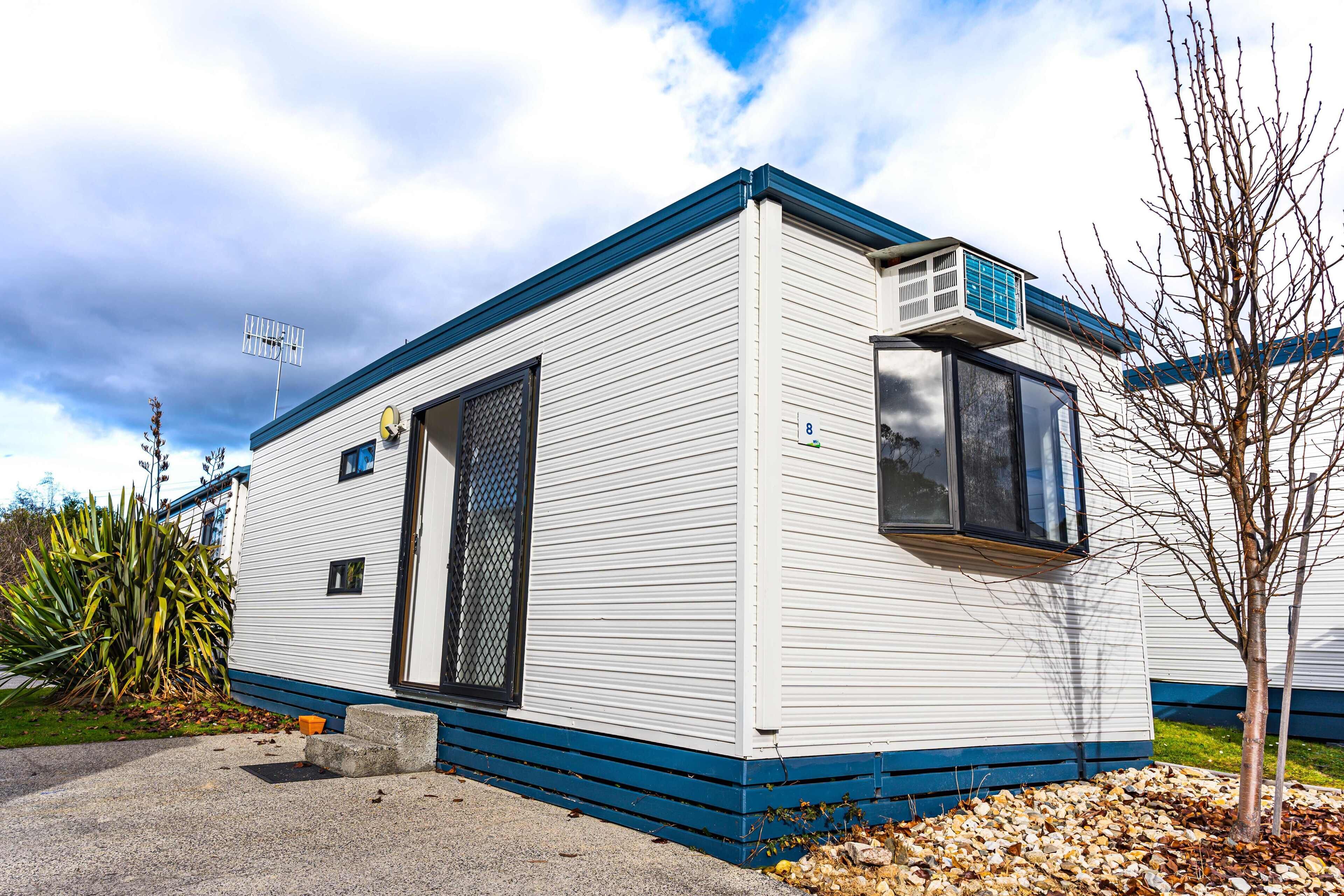 A single-story mobile home with a blue trim, a satellite dish, and a small window.