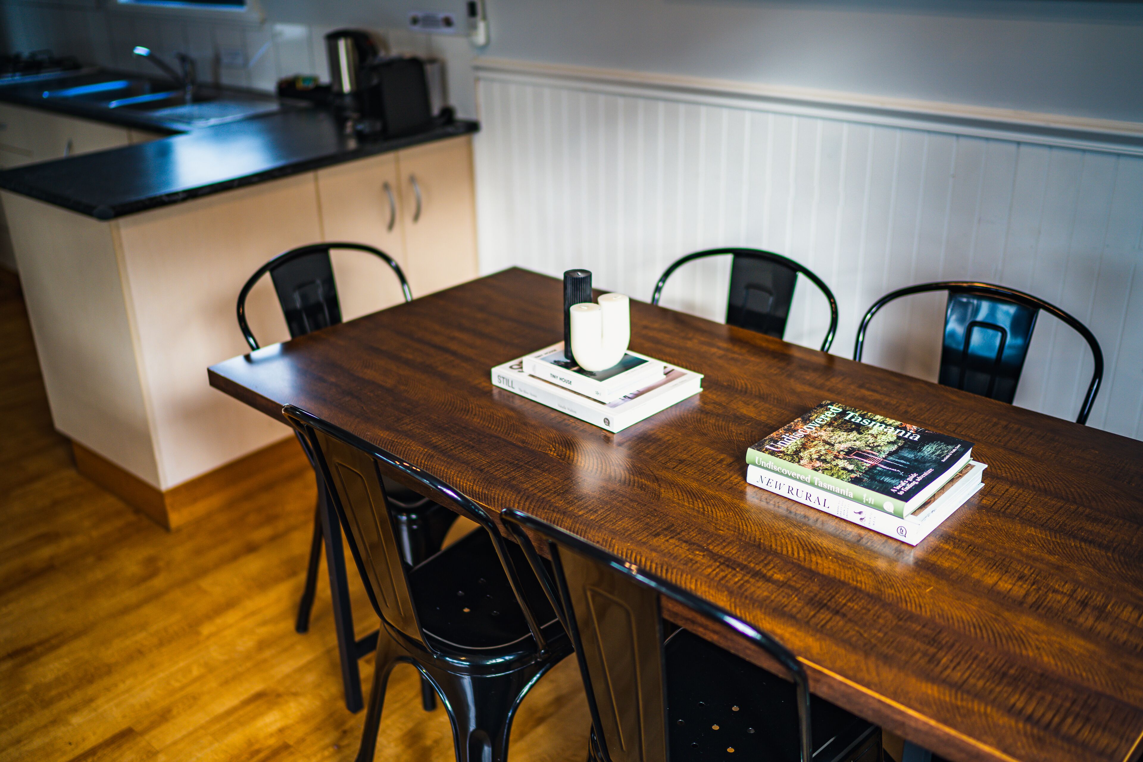 A wooden dining table with four chairs, a book, and a white object on the table.