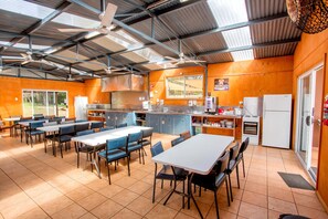 A spacious indoor dining area with high ceilings, multiple tables and chairs, a kitchen area with a refrigerator and stove, and a large window providing natural light. - BIG4 TASSIE GETAWAY PARKS ST HELENS (St Helens)