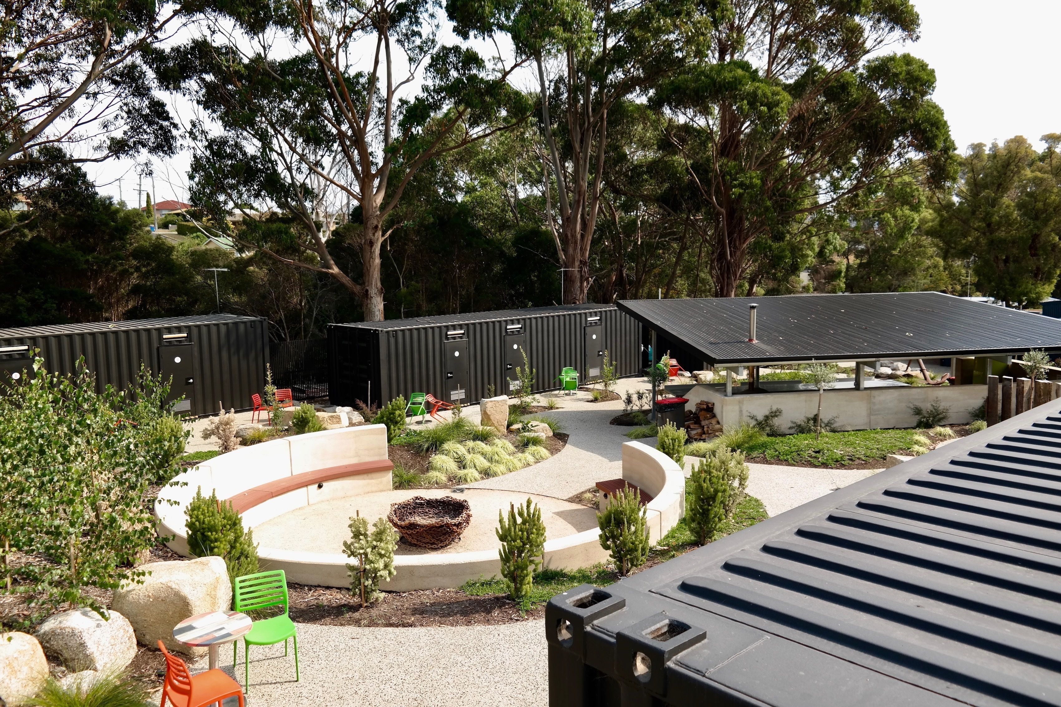 A modern outdoor area with a circular seating area, a covered pavilion, and a view of a residential area in the background.
