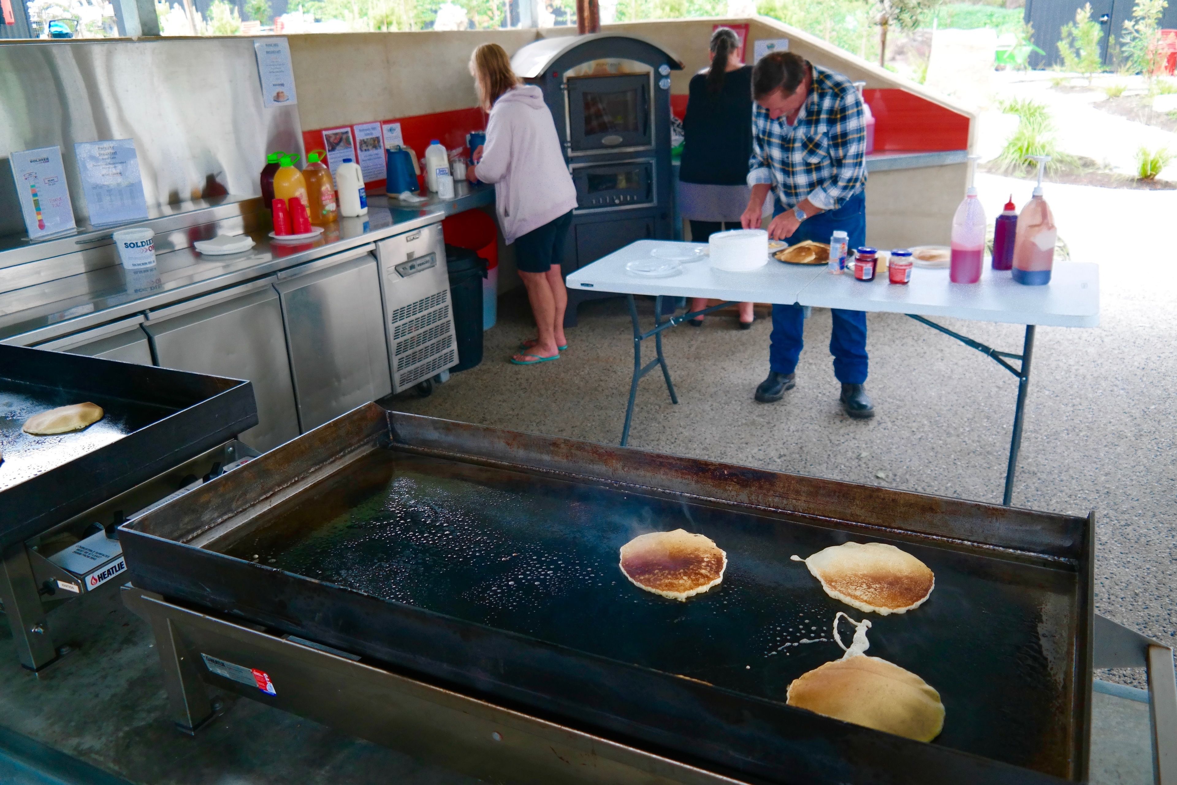 A commercial kitchen with a griddle cooking pancakes, a soda dispenser, and a microwave.
