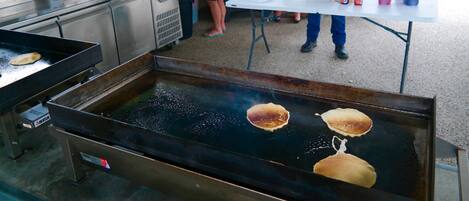 A commercial kitchen with a griddle cooking pancakes, a soda dispenser, and a microwave.
