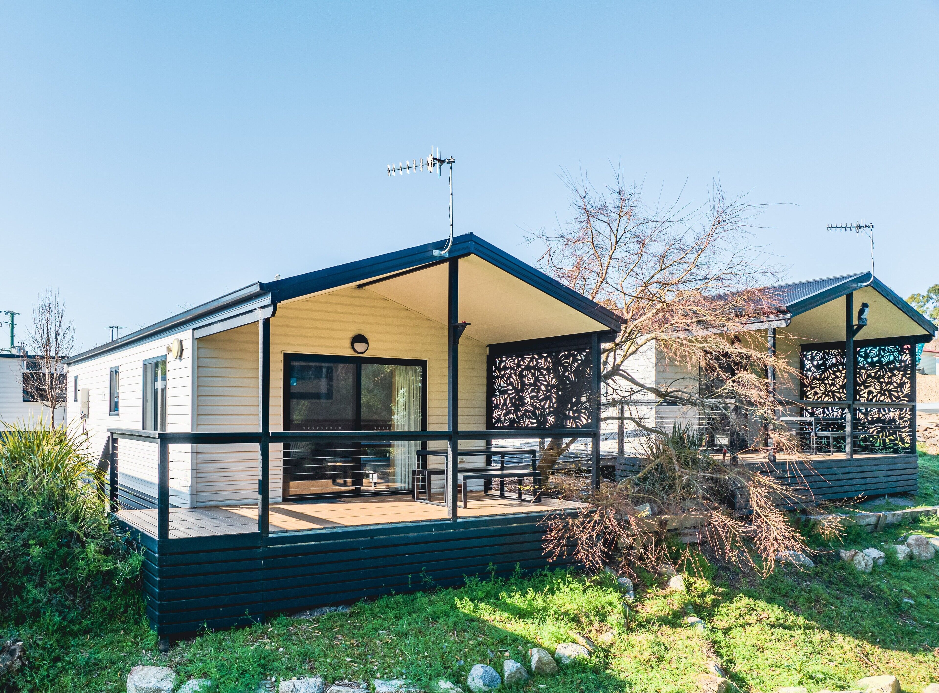 Une maison mobile moderne dotée d’un porche couvert, d’une petite terrasse et d’une grande fenêtre.