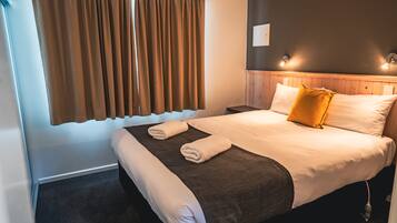 Habitación de hotel con una cama grande, cabecera de madera, dos mesitas de noche y una ventana con cortinas.