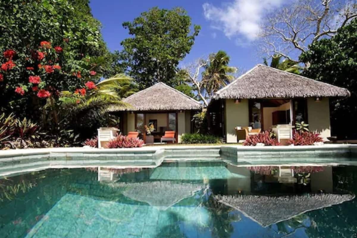 A resort with a clear pool, thatched-roof huts, and lush tropical vegetation.