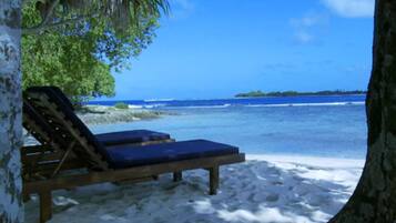A beach scene with a wooden lounge chair and a blue cushion, a sandy beach, and the ocean in the background.