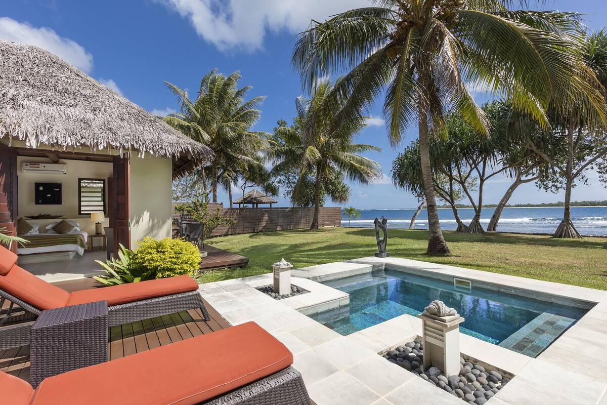 A pool area with lounge chairs, a thatched-roof structure, and palm trees.