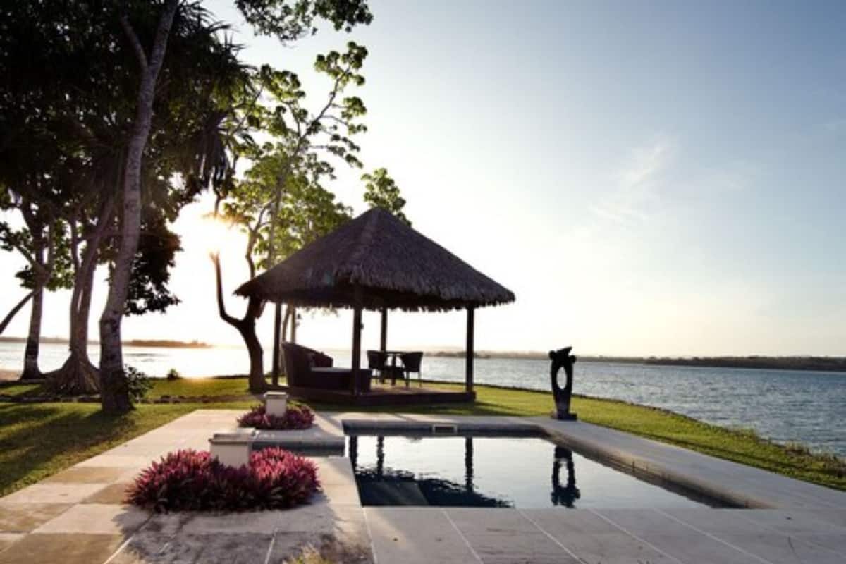 A pool area with a thatched-roof gazebo, surrounded by trees and a view of the water.