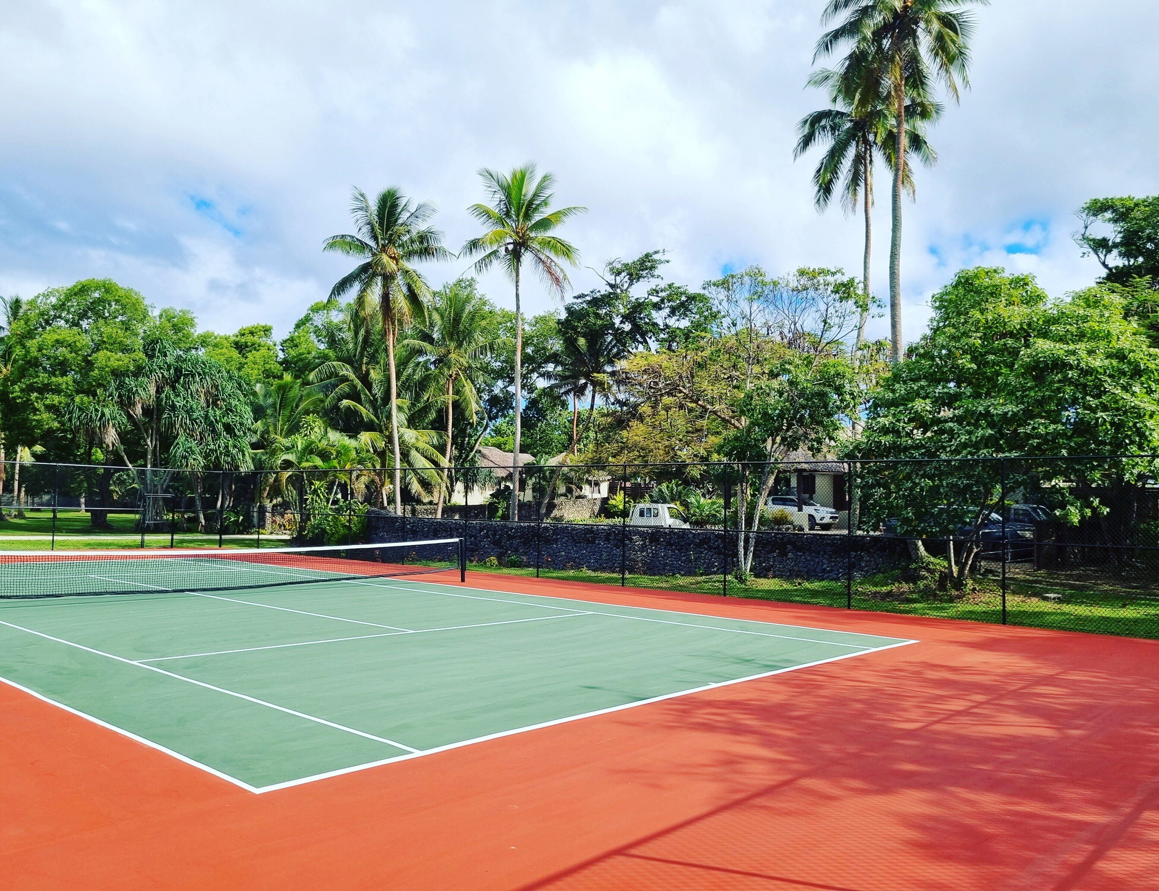 A tennis court surrounded by lush greenery and tall palm trees.