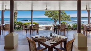 Un espace de restauration en plein air, avec des tables et des chaises, offrant une vue sur une plage et l’océan.
