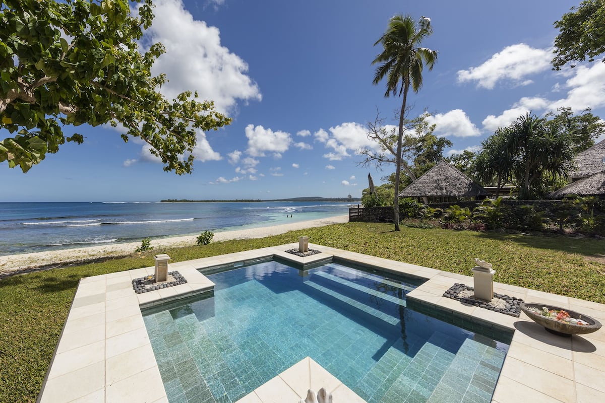 A rectangular pool with clear blue water, surrounded by a well-maintained lawn and a view of the ocean.