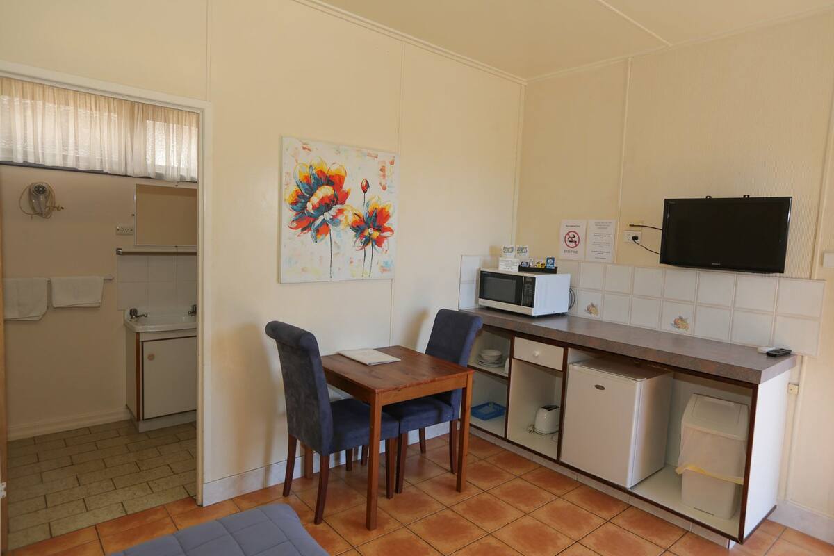A compact kitchen with a dining table, chairs, a microwave, and a TV.