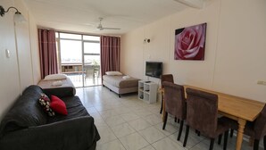 A living room with a sofa, a bed, a dining table with chairs, a TV, and a ceiling fan.