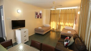 A hotel room with a TV, a sofa, a bed, a dining table, and a ceiling fan.