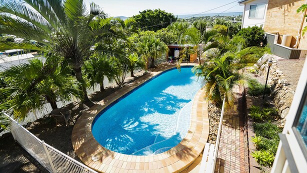 A swimming pool surrounded by palm trees and a brick patio.