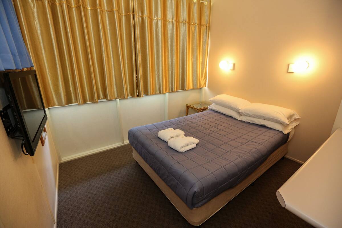 A hotel room with a bed, a small bedside table, a TV, and a window with curtains.