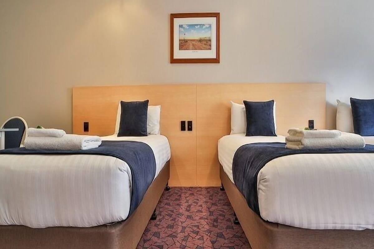 A hotel room with two beds, a wooden headboard, and a framed picture on the wall.