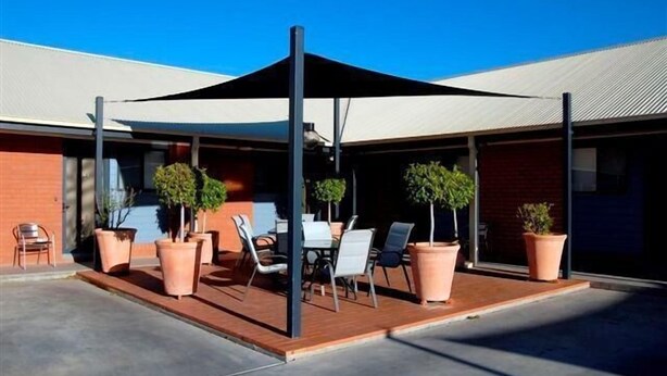 An outdoor patio with a covered seating area, potted plants, and a clear blue sky. - Albert Motel (Moree)