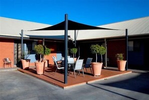An outdoor patio with a covered seating area, potted plants, and a clear blue sky.
