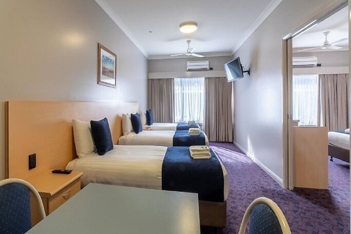 A hotel room with two beds, a desk, a chair, a TV, and a ceiling fan.