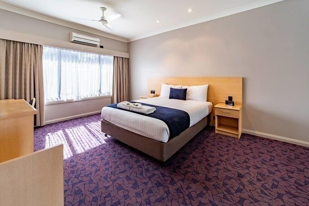 A hotel room with a large bed, a desk, a nightstand, and a window with curtains.
