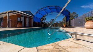A swimming pool with a covered area, a building with a covered entrance, and a fenced area with potted plants. - Albert Motel (Moree)