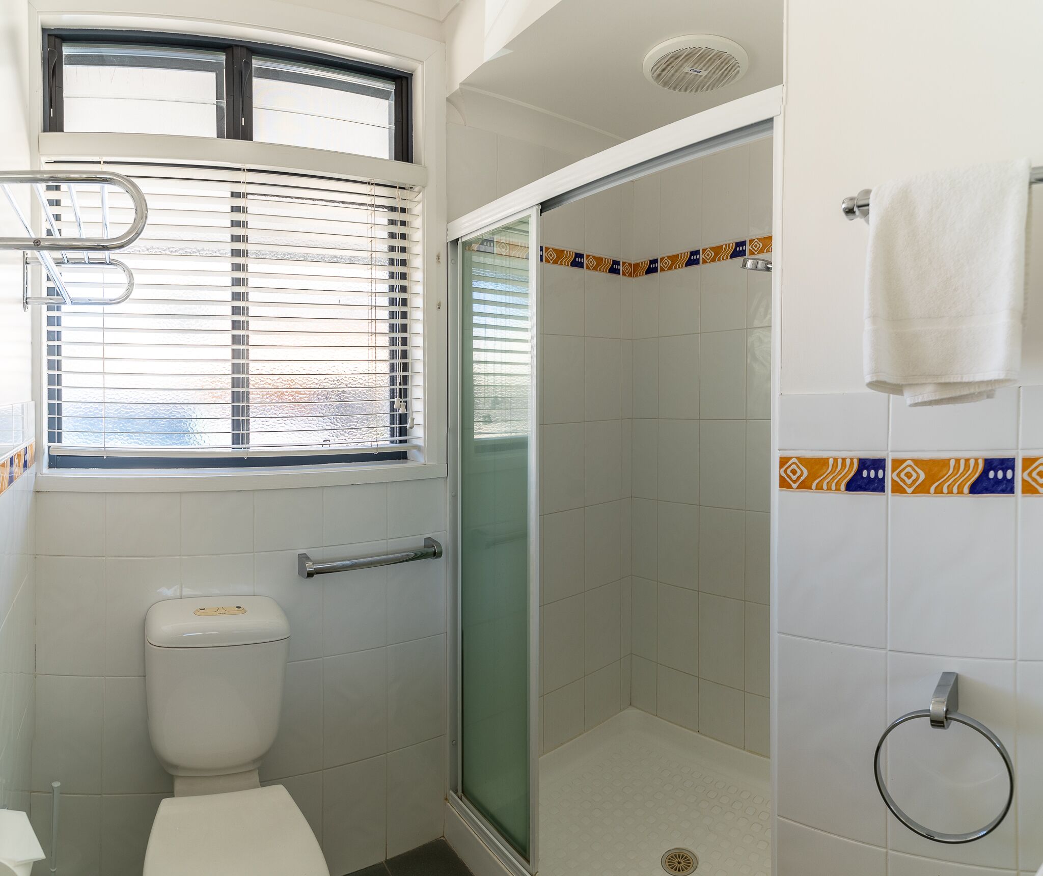 A bathroom with a toilet, a shower with a glass door, and a window with blinds.